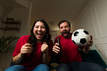 Happy couple cheering for their soccer team watching the game on tv