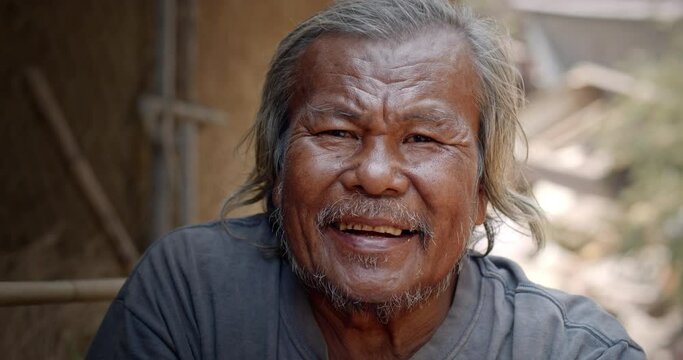 A smiling Asian man who is a homeless ragpicker or has a career collecting garbage and selling it, live in a abandoned house at a slum village.