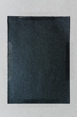A black square on white paper, the center of which is filled with very dark grey glitter dust,...