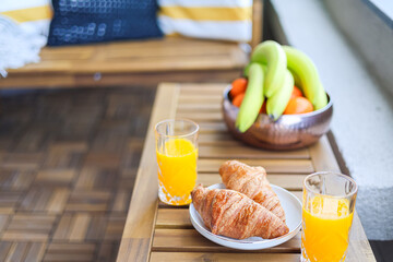 Breakfast at home on the balcony. Close up photo with some croissants, orange juice and fruits placed on a wooden table. Cozy breakfast.