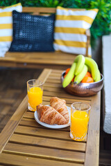 Breakfast at home on the balcony. Close up photo with some croissants, orange juice and fruits placed on a wooden table. Cozy breakfast.