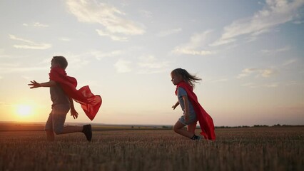 children in superhero costumes. concept of a happy childhood and family for a child. a boy and a girl with red capes and blue T-shirts are running across a lifestyle field, sunset in the background