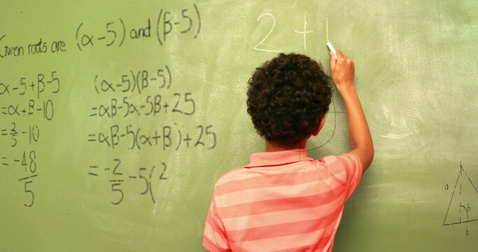 Image of math formulas over back view of biracial boy writing on black board