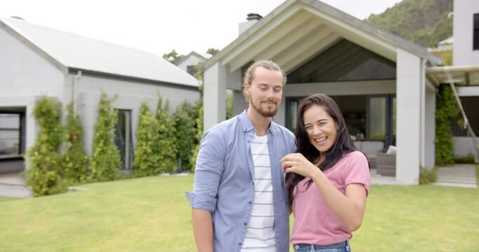 A young diverse couple is smiling outdoors in the backyard at home, holding keys