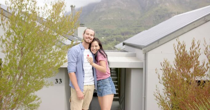 A young biracial couple is standing outside a new home showing key