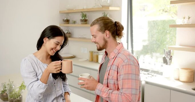 A diverse couple enjoys a warm drink in the kitchen at home