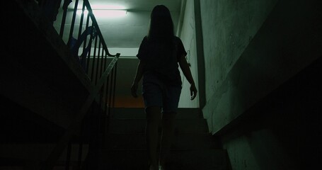 A woman ghost is walking down a dark stairwell. The image has a moody scary horror creepy darkness...