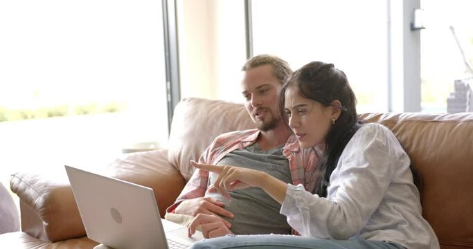 A biracial couple is using a laptop at home on the couch