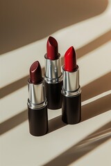 Three red shade lipsticks in tubes against beige background in sunlight