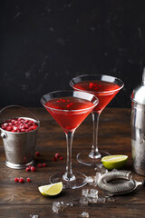 Two glasses of Cosmopolitan cocktail with frozen cranberries, slices of lime and crushed ice on wooden table