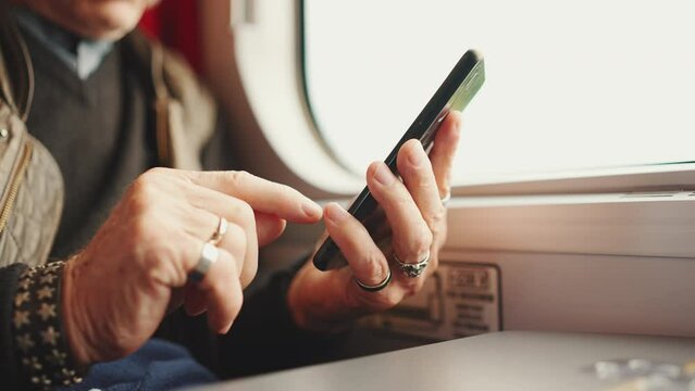 Close-up of old man's hands using smartphone in train while traveling. Senior travels on a train and uses a mobile phone, Slow motion