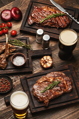 Wooden table served with various grilled meat, vegetables and glasses of beer. Striploin steak,...