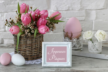 Arrangement avec des fleurs et des œufs de Pâques colorés avec le texte Joyeuses Pâques.
