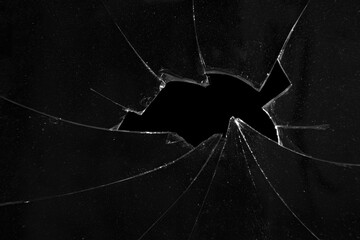 Cracks of broken glass, black background texture of a hole in a window.