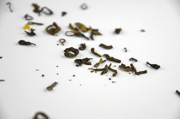 Small pieces (leaves) of dry green tea on a white background, closeup macro, side view