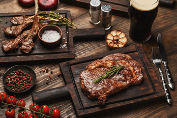 Wooden table served with various grilled meat, vegetables and glass of beer. Ribeye steak and lamb...