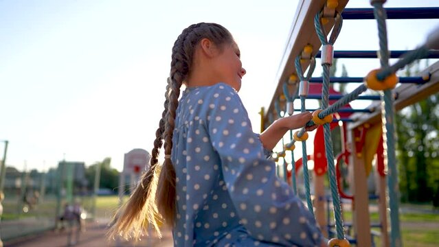 child plays on the playground. concept of a happy childhood and loving family. a child smiles joyfully and climbs a ladder on a playground, the glare lifestyle of the sun in the background