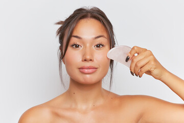 Close-up of Asian girl with gua sha massage stone holding at her face looking with gentle smile, skincare product concept, copy space