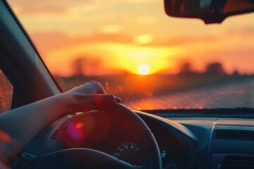 The silhouette of a person's arm and hand resting on the steering wheel of a car, with the warm glow of a sunset or sunrise visible through the windshield, suggesting a relaxed driving experience.
