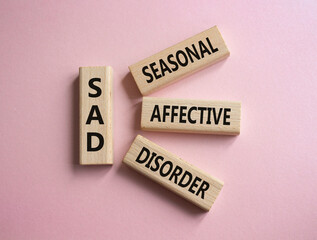 Sad - Seasonal Affective Disorder symbol. Wooden blocks with words Sad. Beautiful pink background....