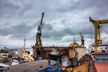 Fototapeta na wymiar Industrial ship repair yard with floating dock, vessels undergo maintenance. Tugboats assist in marine operations, heavy cranes lift equipment. Overcast sky over maritime workplace, shipping industry