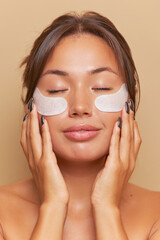 Portrait of young woman with under eye patches smiling happily and touching her face, skincare product concept, copy space