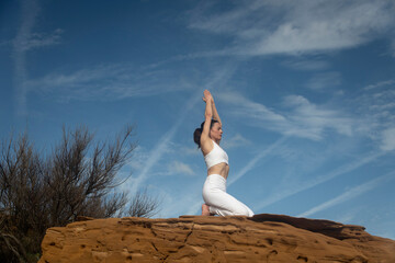 woman kneeling outside on red rocks, meditating and practicing yoga. Serenity