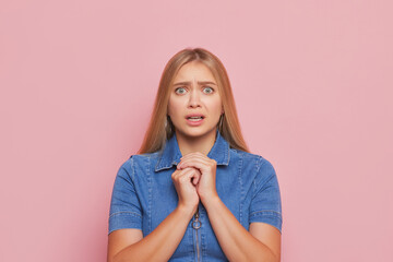 Pretty girl with long hair in blue shirt stands over background pressing hands to her chest, good day concept, copy space