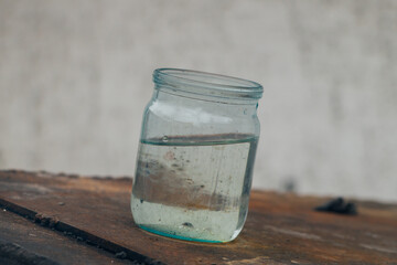 An old glass jar with water stands on a rusty surface