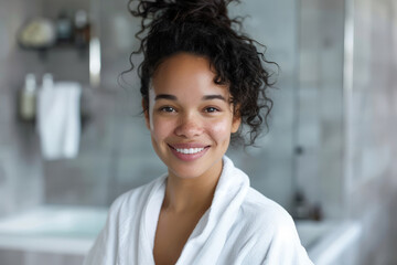 A biracial woman is smiling while wearing a white bathrobe in a bathroom