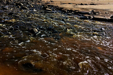 A close-up of water flowing over rocks, illuminating the wet surfaces under bright light.