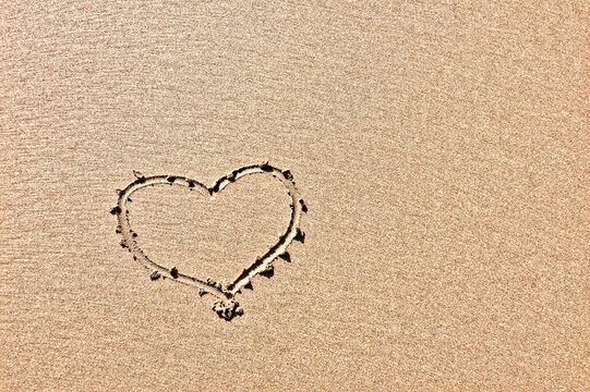 The photo captures a heart outline drawn in sand, highlighting its texture.
