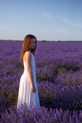 Profile portrait of a young girl poses in a field of lavender flowers at sunset.