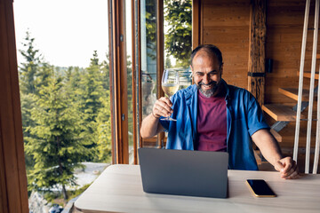 Man having a virtual toast during video call in a home with forest in the background