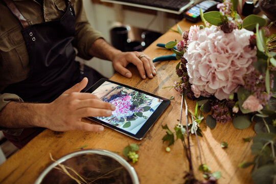 Male florist taking pictures of bouquet on tablet in flower store