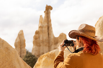 A woman wearing a cowboy hat is taking a picture of a mountain. The photo has a rustic, adventurous...