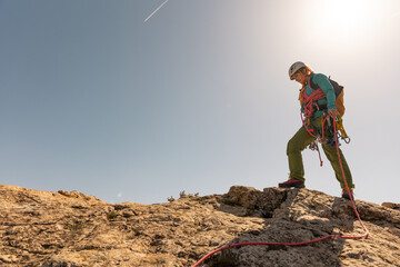 A woman is climbing a mountain with a red rope. The sky is clear and the sun is shining brightly