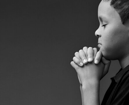 boy praying to God with hands together on grey black background with people stock image stock photo