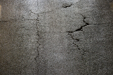 Cracks in the asphalt at night, illuminated by car lights.