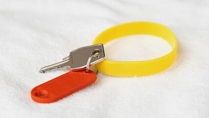 Yellow rubber bracelet and a key with a red tag lie on a white terry towel. Key to an individual...