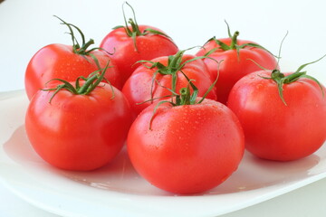 Lots of fresh ripe red tomatoes covered with water drops on a white background. Isolated. Close-up.