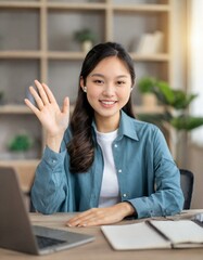 Young and energetic female is ready for an online interview on a video call, sitting at the desk at home and looking and waving at the camera, saying hello. Job hunting concept
