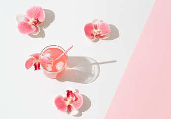 Summer scene made with pink tropical refreshing drink and orchid flowers on white and pink background. Sun and shadows. Minimal cocktail concept. Trendy summertime party idea. Summer aesthetic.