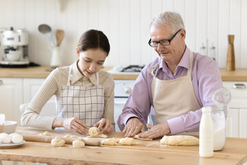 Elderly grandfather teaching pre-teen granddaughter to cook, multi generational relatives wear...