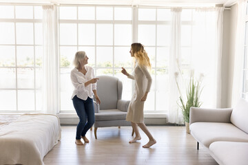 In fashionable light spacious living room active family dancing, mom and teen daughter moving to...