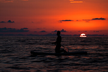 A man swimming in a boat in the sea at a beautiful red sunset