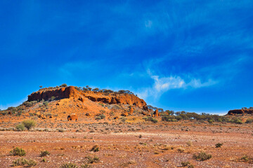 Fototapeta na wymiar Red laterite (rocks with iron and aluminium) formations surrounded by saltbush and mulga in the desert near Mount Magnet, Western Australia. 