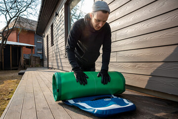 Man folding an inflatable stand-up paddleboard (SUP) on a wooden deck next to a modern home