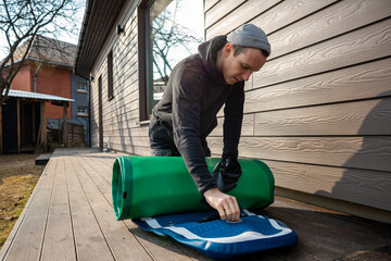 Man folding an inflatable stand-up paddleboard (SUP) on a wooden deck next to a modern home - obrazy, fototapety, plakaty