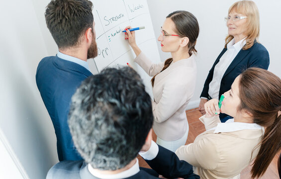 Side view of an intelligent female business expert conducting a SWOT analysis during an interactive meeting between the decision makers of a successful company